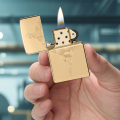 Złota zapalniczka Zippo trzymana w dłoni z wyciętym motywem węża widocznym na obudowie