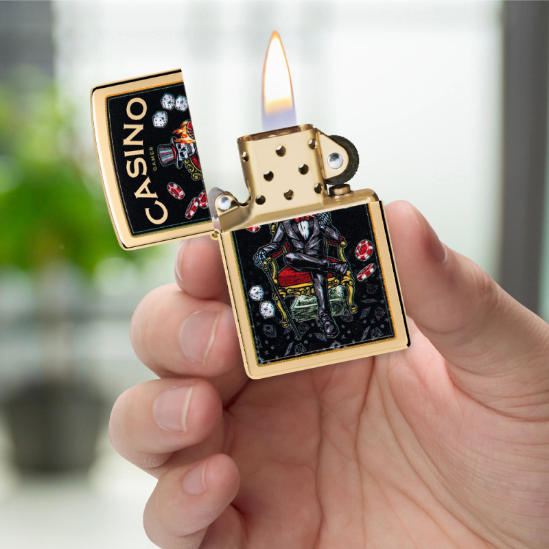 Złote Zippo znajdujące się w dłoni z charakterystyczną kasynową kompozycją na ciemnym tle