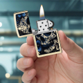 Złota Zippo z motywem czaszki i kwiatów prezentowana w dłoni